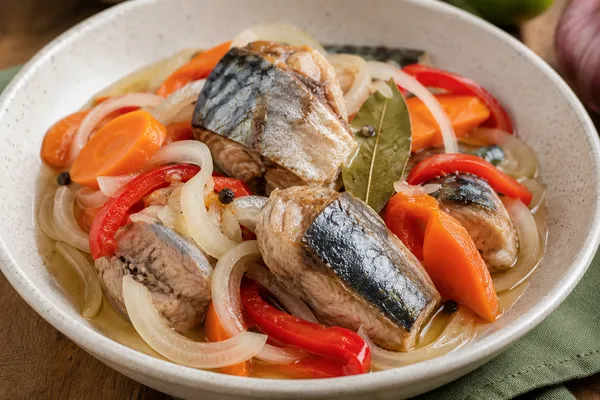 Fotografía del platillo caballa en escabeche servido en un tazón color blanco puesto sobre una mesa de madera.